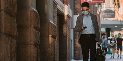 Man wearing face mask walking down the street and checking his phone