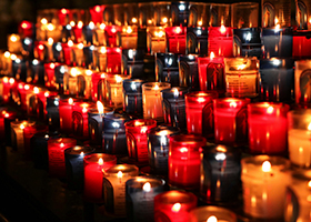 Rows of lit candles in red, purple and yellow glass jars